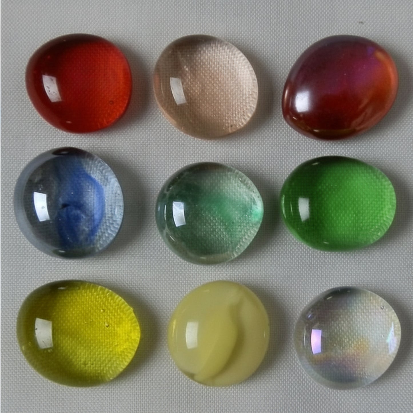 Nine colorful marbles slightly flattened (Energy Cells) on a textured surface