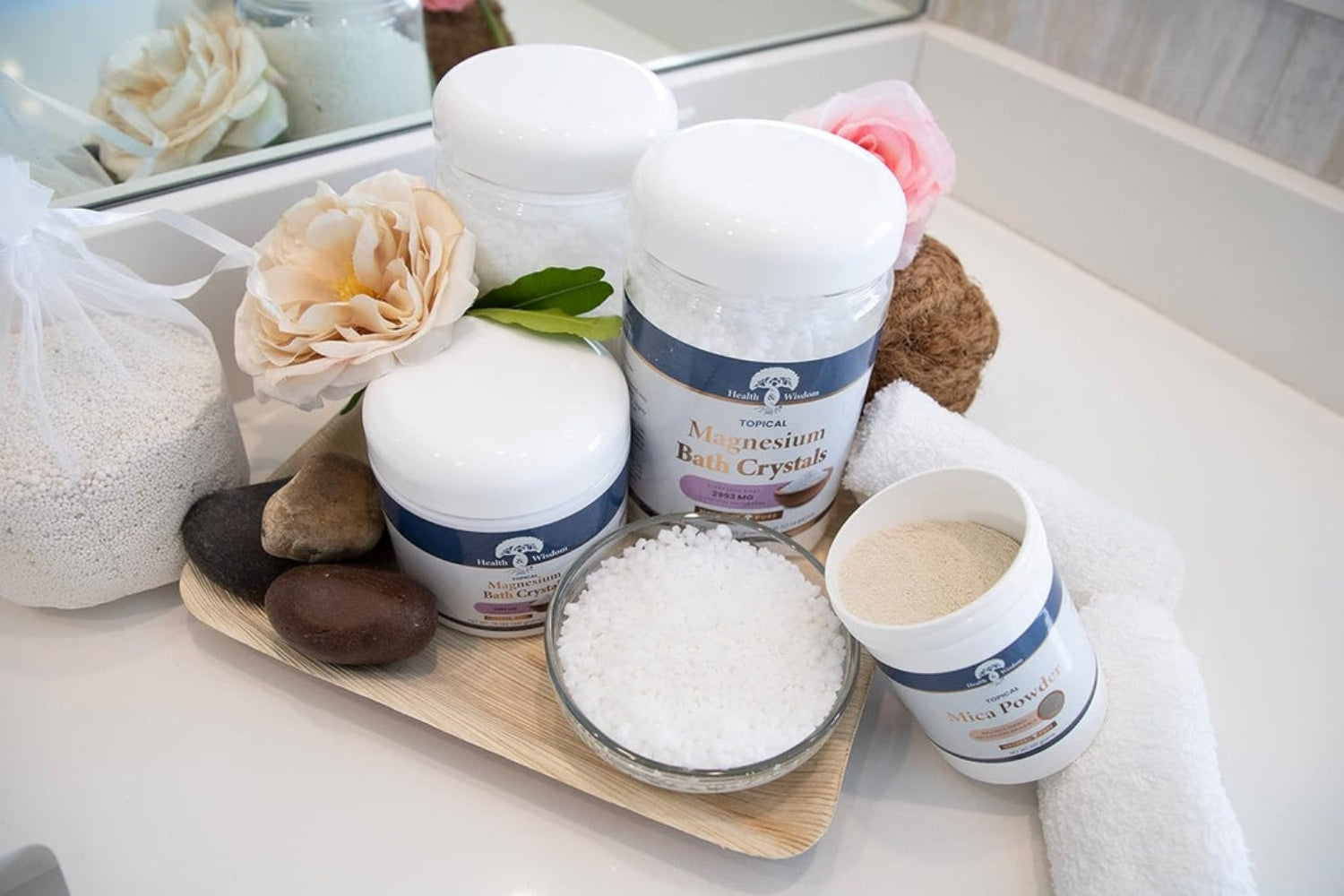 Bath products including bath bombs, crystals, and salts on a tray with flowers and stones.