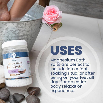 Bottle of magnesium bath crystals with Uses and a bucket of water, rose, and stones on a light background.